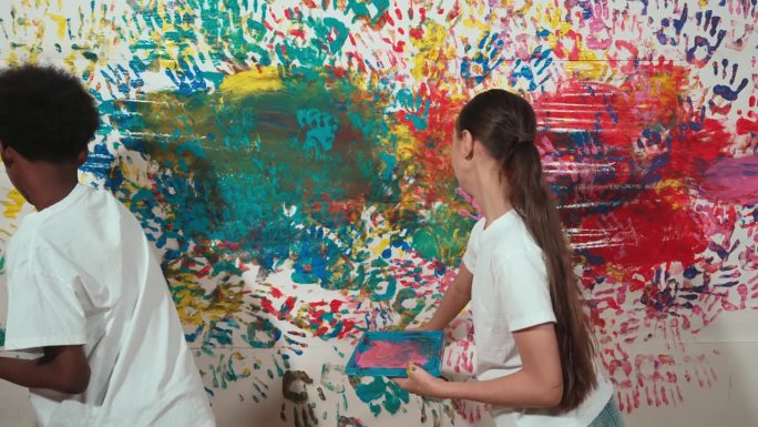 年轻可爱的学生用手画彩色的染色墙。启迪