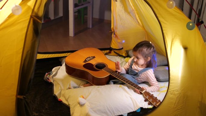 小女孩在棚屋里弹吉他。爱好音乐的孩子