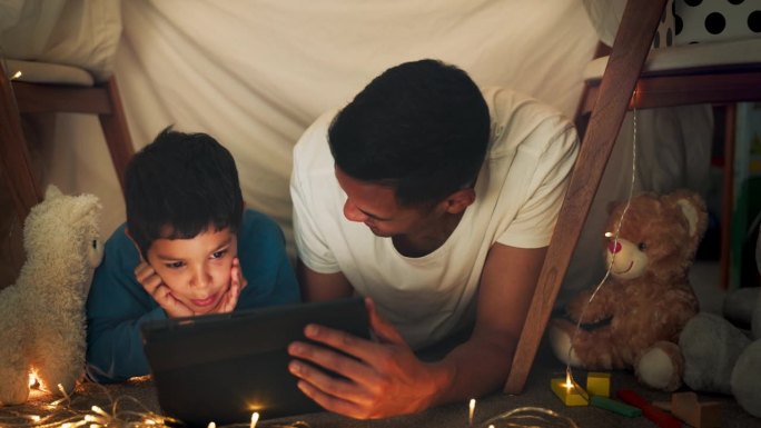 晚上，父子俩在帐篷里用平板电脑看电影，在毯子堡里玩网络游戏和卡通片。童话般的灯光，家庭和快乐的爸爸带