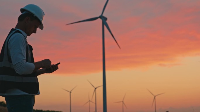 日落时分，SLO MO工程师在乡下的智能手机上检查风力涡轮机的运行数据