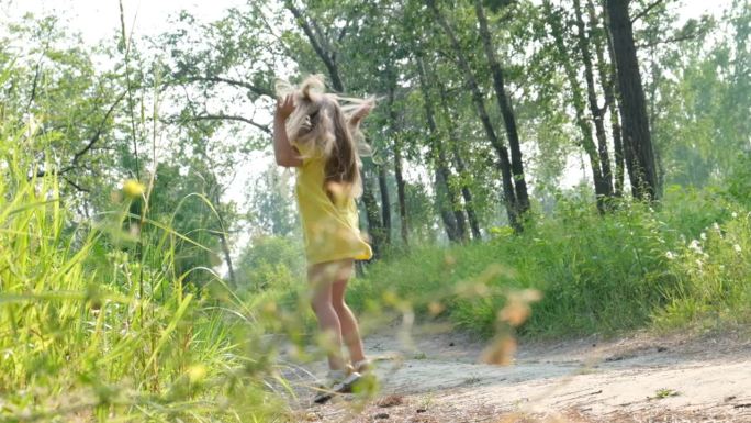 快乐的小女孩，金色的长发，穿着黄色的裙子，沿着草地上的小路奔跑，夕阳西下