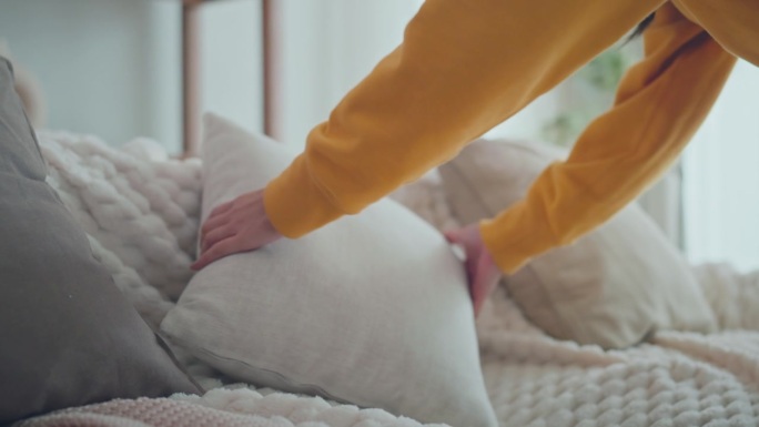 女人的双手在舒适的沙发靠垫上排列枕头，在家里，家务和清洁的概念