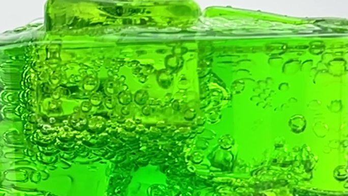 近距离倒软饮料，绿色苏打泡沫与冰到玻璃隔离