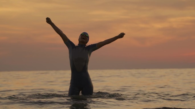 日落时，在海里游泳的活跃女子举起手臂的慢镜头镜头