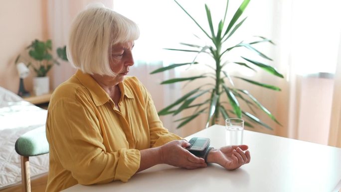 一位老妇人正在家里用数字血压计测量自己的血压和心率。老年妇女照顾健康。健康和医疗的概念。