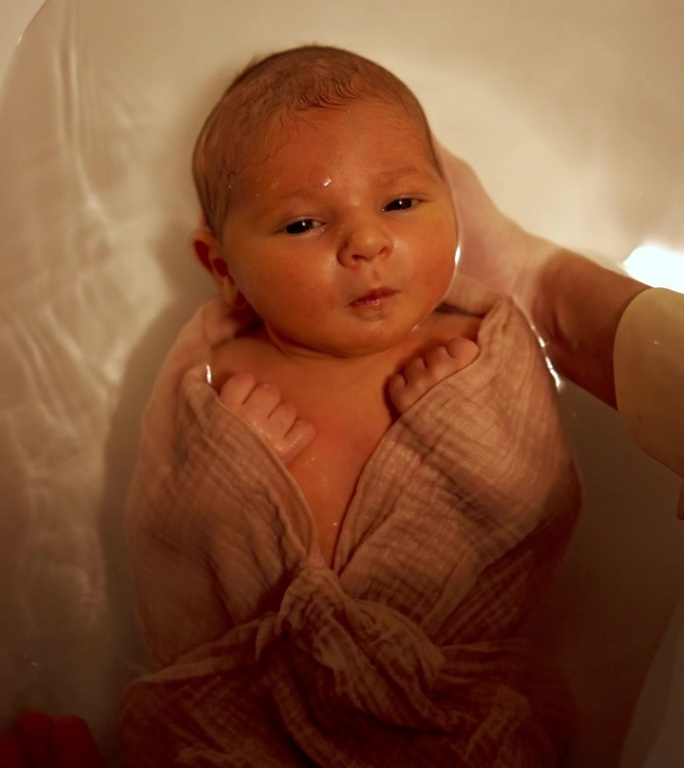 小婴儿躺在浴缸里的水里。俯视图宝宝第一次洗澡。垂直视频
