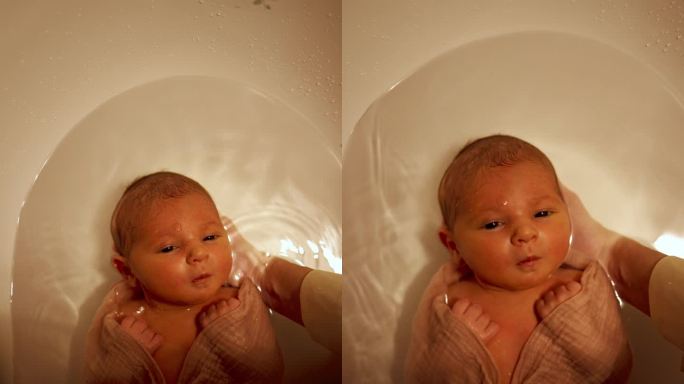 小婴儿躺在浴缸里的水里。俯视图宝宝第一次洗澡。垂直视频