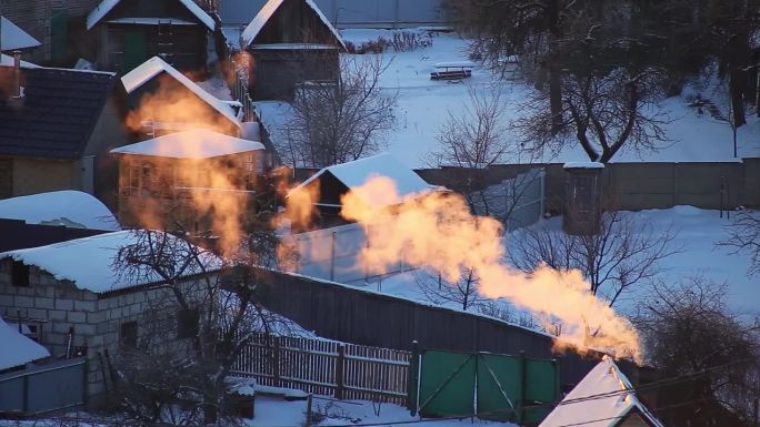 橙色的烟雾和蒸汽从村舍屋顶的烟囱里冒出来，映衬着冬日的晨曦。村子里一个寒冷的冬日早晨。