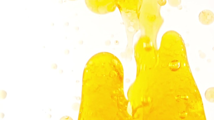 慢动作移动的金黄油，气泡在水中上升在浅白色的背景。带有气泡的透明化妆品凝胶液。微距镜头。