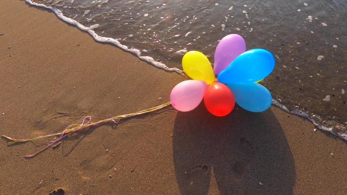 一束五颜六色的气球躺在沙滩上的海滩与海浪在阳光明媚的早晨和晚上。休闲娱乐娱乐休息娱乐庆祝节日节日。慢