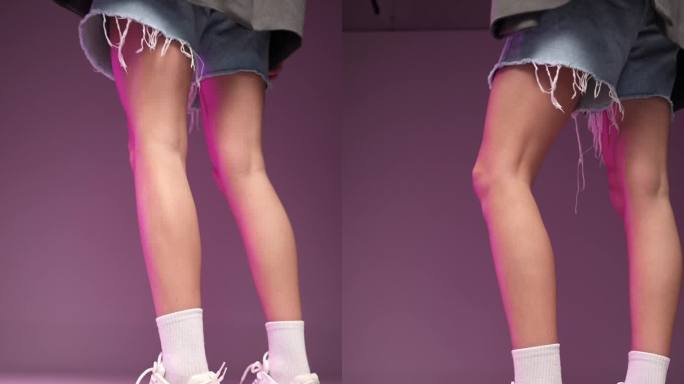 工作室里穿着牛仔短裤和白色运动鞋的女性腿，背景是粉红色的。垂直视频