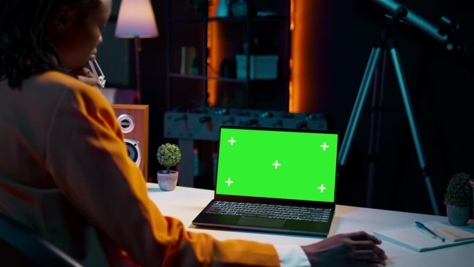 年轻女子在她的家庭办公室使用带有孤立绿屏显示的笔记本电脑