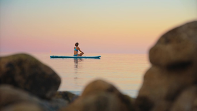 在日落的海洋中，活跃的女性在冲浪板上练习瑜伽
