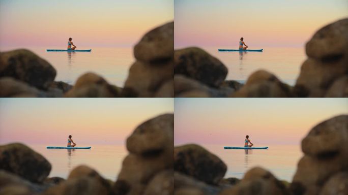 在日落的海洋中，活跃的女性在冲浪板上练习瑜伽