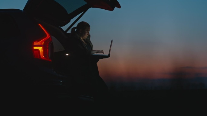 日落时分，孕妇靠在汽车后备箱上使用笔记本电脑的锁定镜头