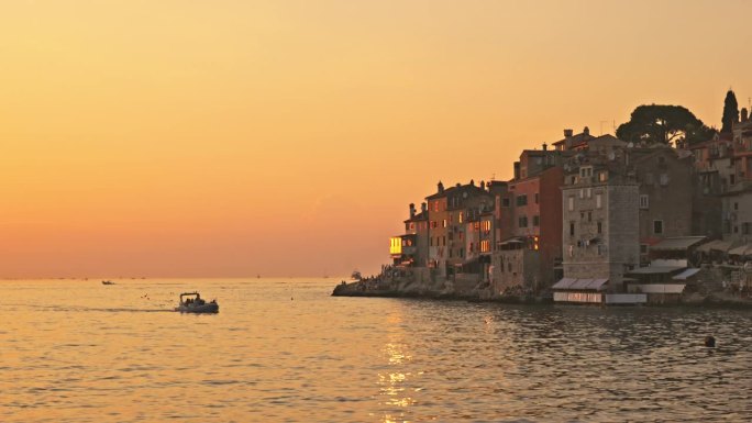 船在海洋中航行，背景是古老的城镇，背景是橙色的天空。罗维尼，伊斯特拉，克罗地亚。