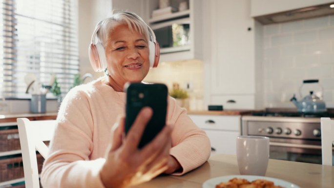 耳机、手机和老女人在厨房里听音乐、专辑或播放列表。快乐，跳舞和老年女性在家里在社交媒体或互联网上播放