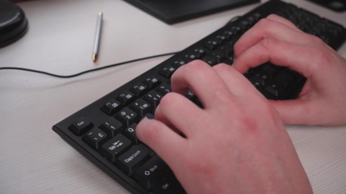 男性的双手在黑色的有线电脑键盘上合上，正在输入信息