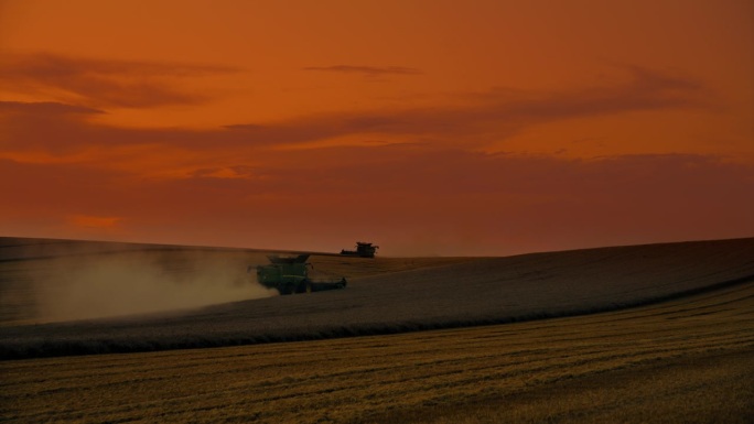 日落时分，联合收割机在小麦景观上对着戏剧性的天空的起重机镜头