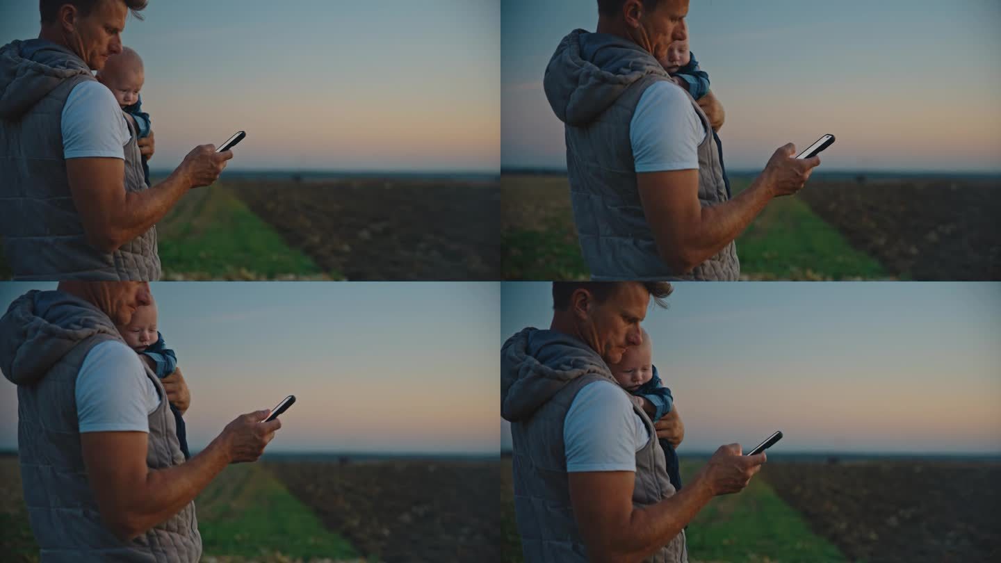 日落时分，男子抱着小男孩站在野外使用智能手机