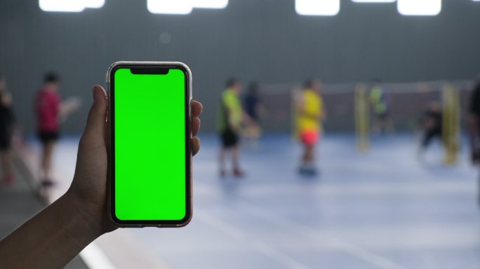 手拿着绿色屏幕的手机在羽毛球馆里