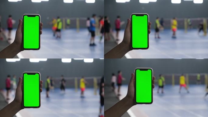 手拿着绿色屏幕的手机在羽毛球馆里