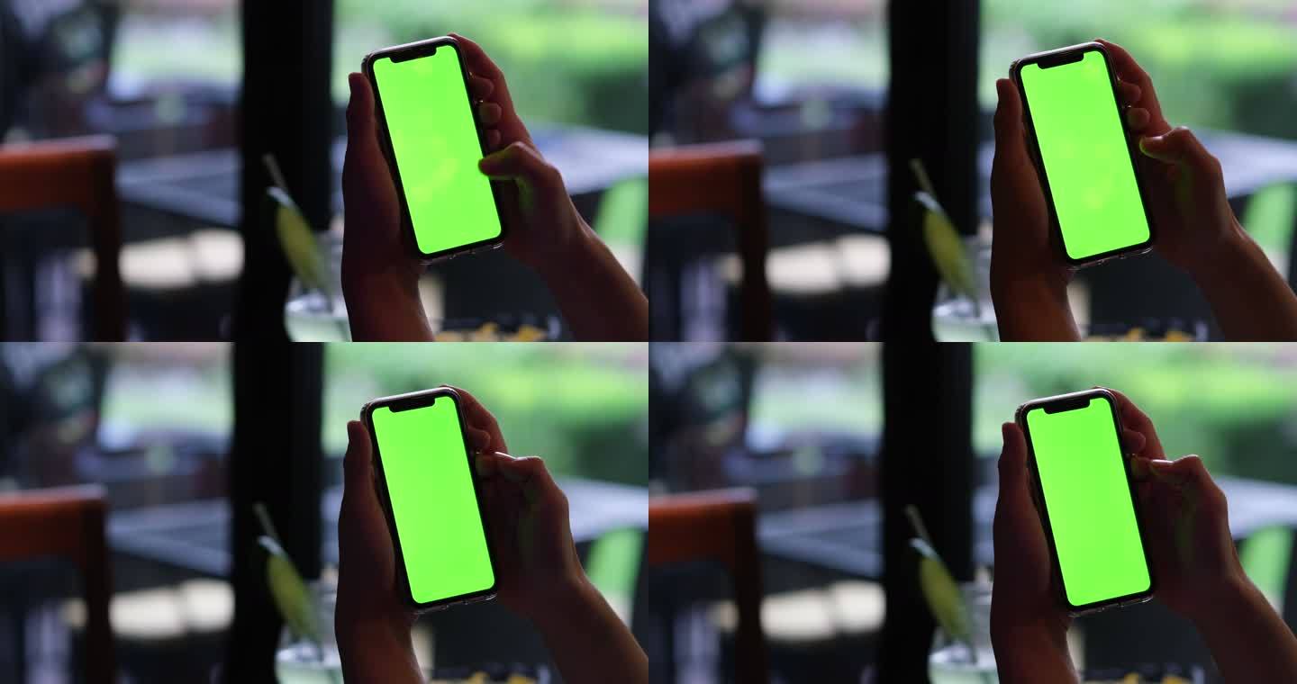手在餐馆里点击和滑动绿色屏幕的智能手机