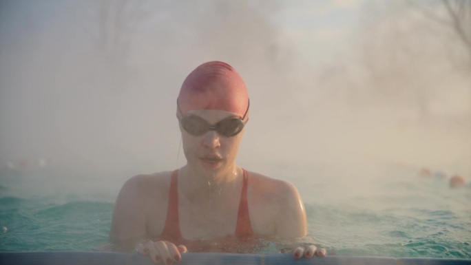 美丽的运动女子在雾蒙蒙的早晨在度假村的游泳池游泳