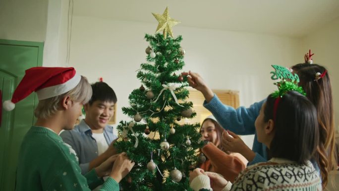 亚洲青年男女组团在家中装饰圣诞树，营造节日气氛