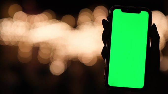 手展示绿屏的智能手机，美丽夜晚的光斑