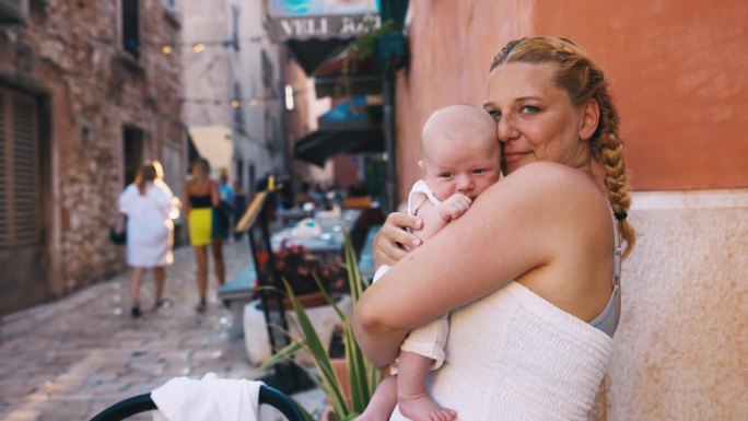 度假期间，快乐的女人抱着可爱的婴儿站在城市街道上。罗维尼，伊斯特拉，克罗地亚。