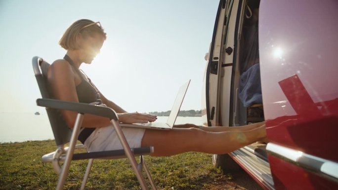 女自由职业者坐在野营车外的椅子上用笔记本电脑工作