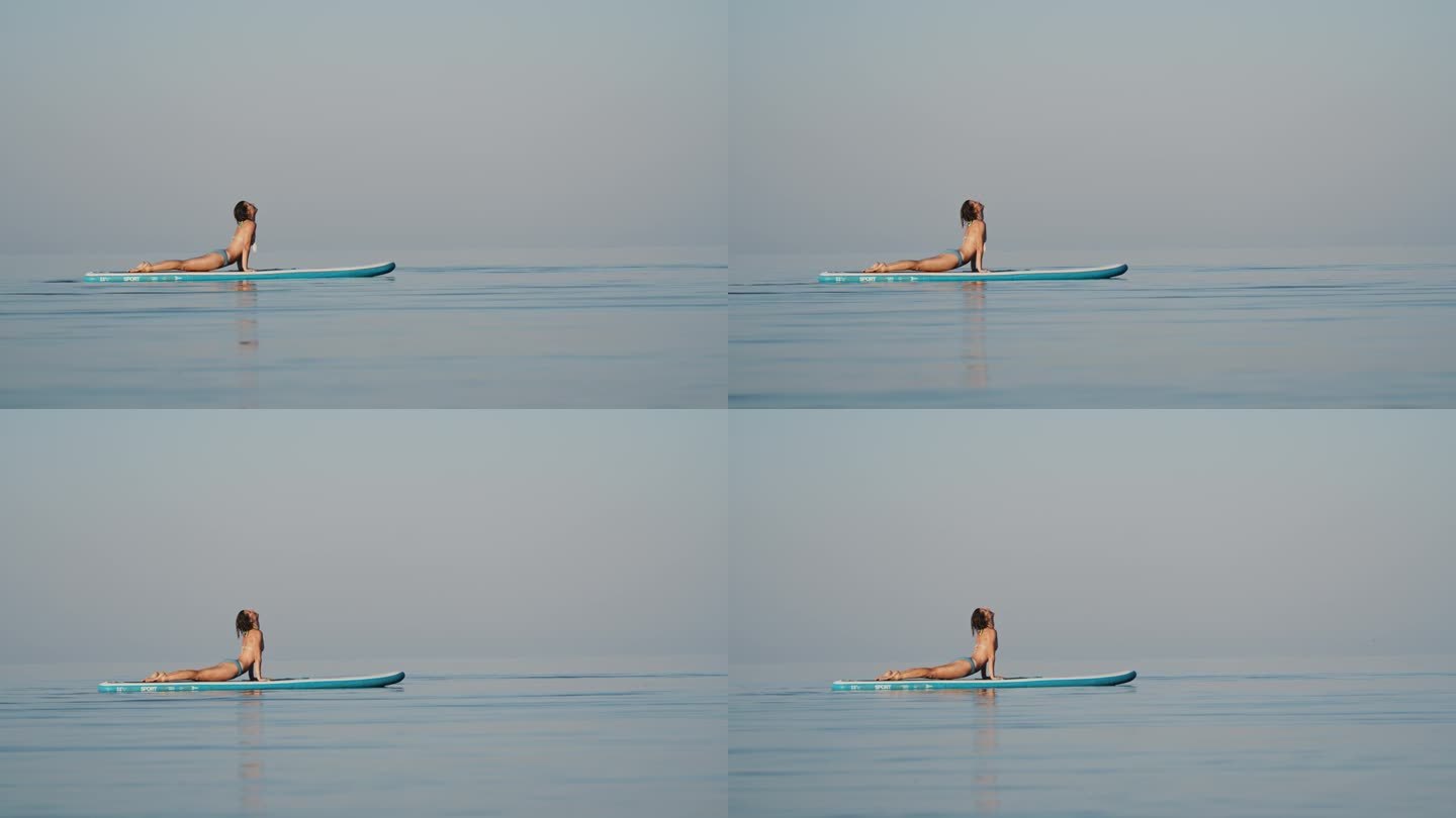 柔韧的比基尼女子在海上冲浪板上练习瑜伽的慢镜头