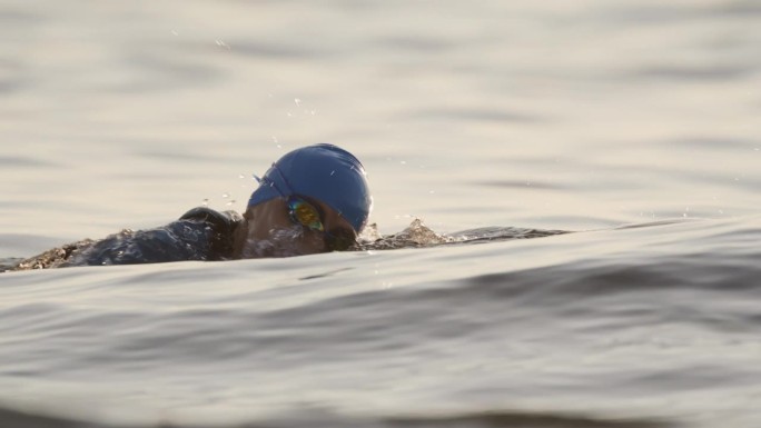 日落时在海洋中游泳的活跃女性的慢镜头镜头。一个女人正在海里游泳。