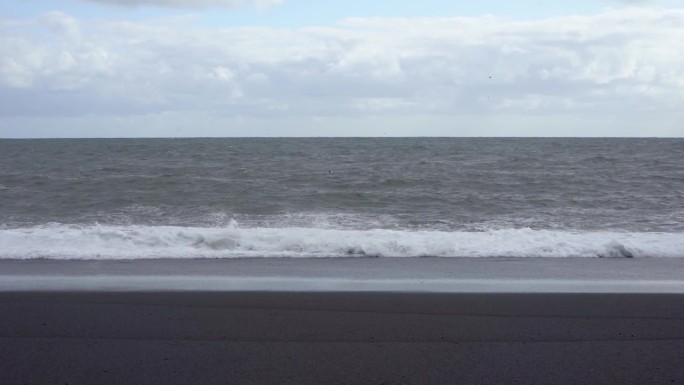 多云的天空下，海浪拍打着冰岛的黑沙滩