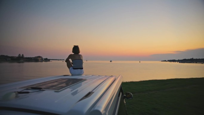 SLO镜头的女人坐在露营车的顶部，并在度假期间看日落的看法