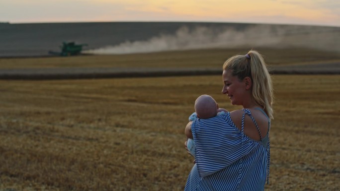 女农学家扛着儿子，看着拖拉机在夕阳下犁地