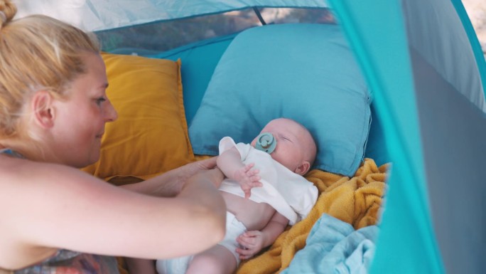 露营时，母亲给躺在帐篷里的小男孩脱衣服