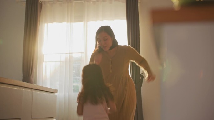 一位亚洲母亲和她的女儿在家里的厨房里跳舞