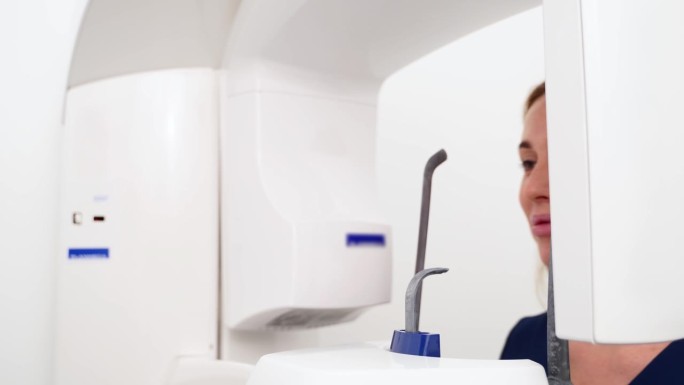 现代牙科门诊女患者做牙齿全景x光片。女病人在医院医疗柜的x光机扫描仪前。年轻女子正在拍摄下巴全景。特