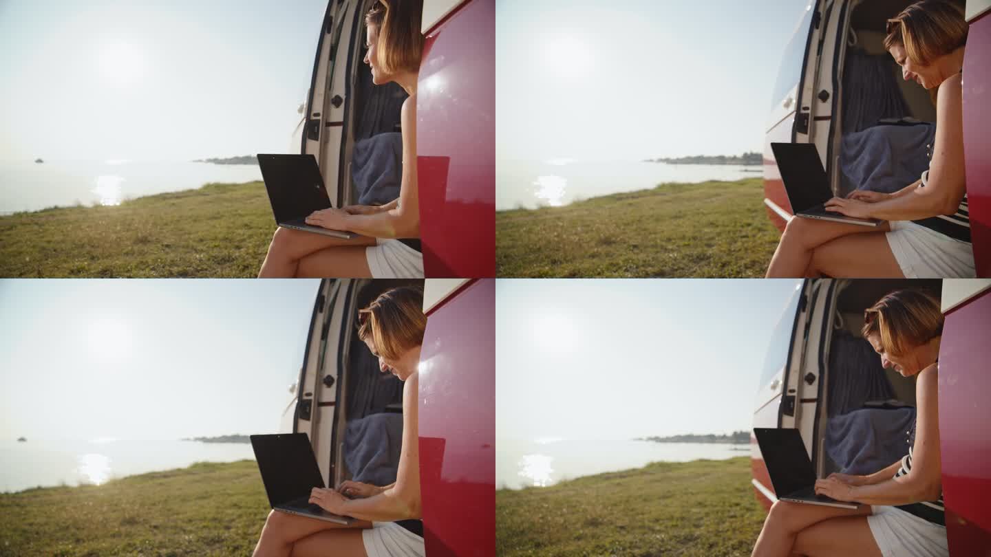 湖岸露营车里微笑的女自由职业者使用笔记本电脑的慢镜头