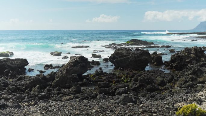 拍拍大海上的黑色岩石，在海边溅起浪花，动感十足