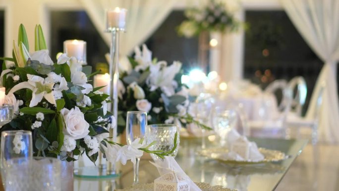玻璃桌，中间饰有天然树叶和白玫瑰，烛台和婚礼玻璃器皿。