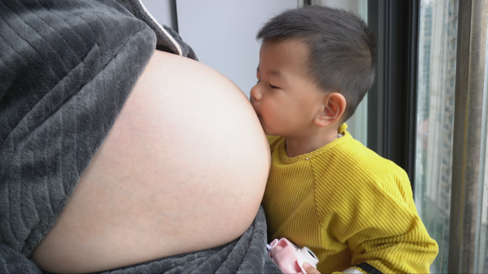 孕妇在窗台晒太阳抚摸肚子小孩过来轻吻肚子