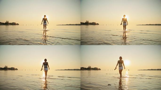 女子在度假期间在日落海滩浅水中散步的慢镜头