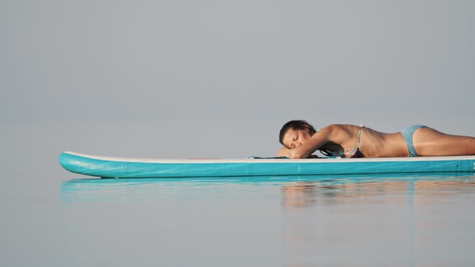 在阳光明媚的日子里，女子在海洋的冲浪板上放松的慢镜头