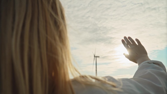 展望明天:一名女子向远处的风力涡轮机和灿烂的太阳伸出手