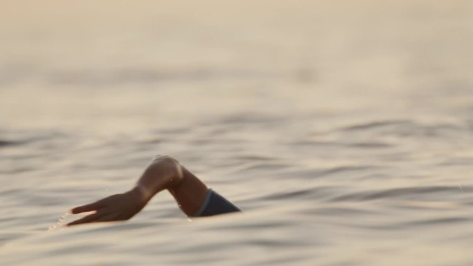 在日落时在海里游泳的度假女性的SLO镜头