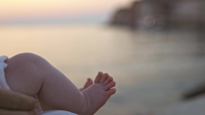 在日落的海边，顽皮的幼儿悬挂着双腿的特写镜头