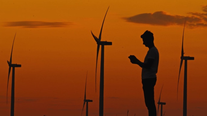 黄昏任务:工程师在黄昏时分用他的智能手机监测风力涡轮机的进展。清洁能源。